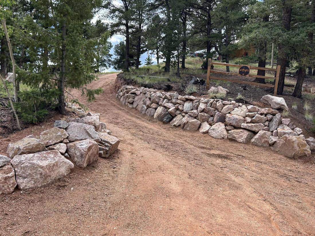 Long dry-stacked natural boulder retaining wall following a curving mountain driveway