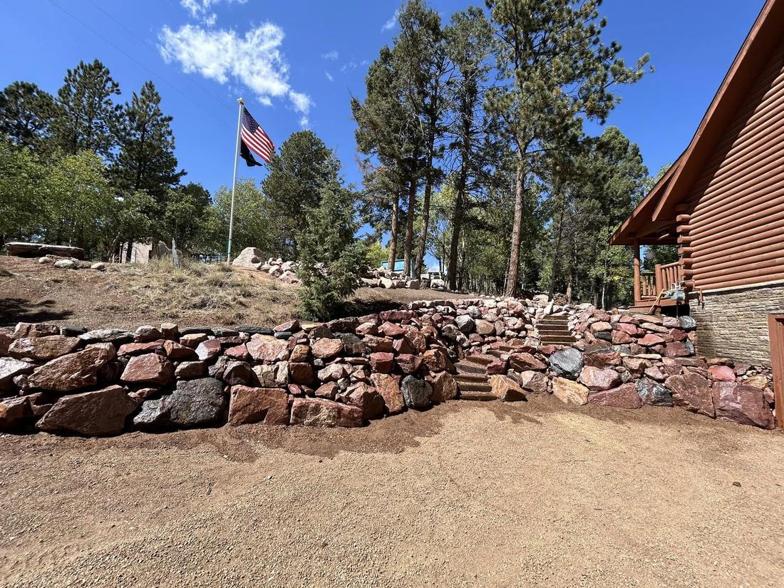 Natural boulder retaining wall with integrated stone steps leading up to a log cabin home