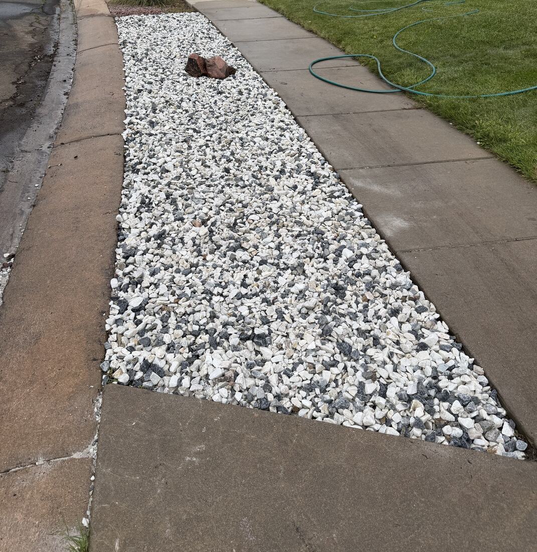 Decorative white and black rock landscaping bed along a walkway