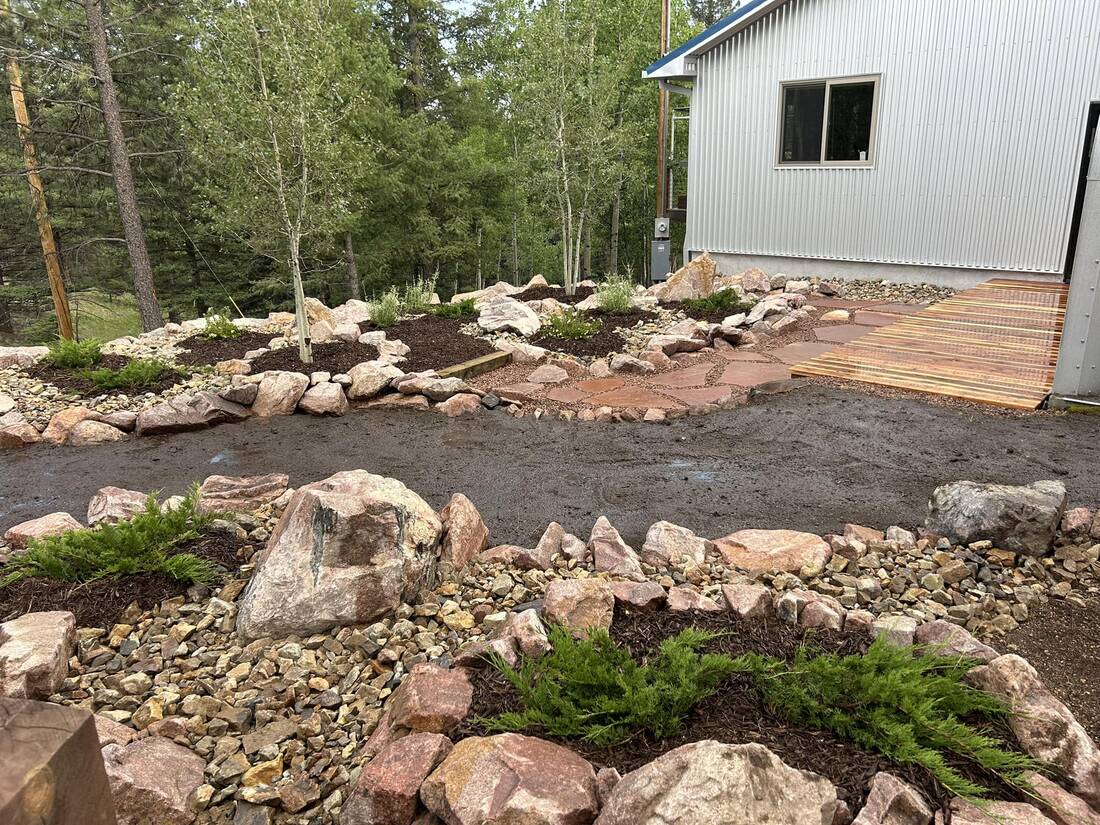 Boulder-bordered planting beds with aspen trees beside a gravel driveway