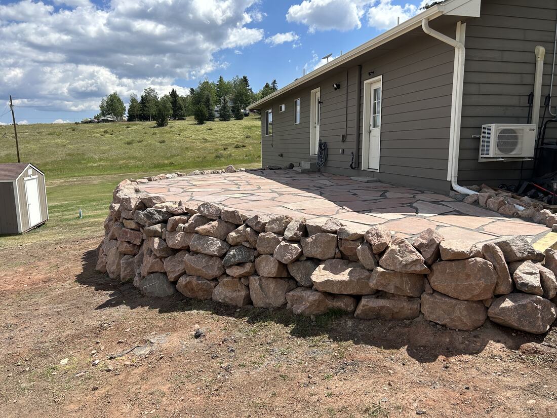 Raised flagstone patio held by a tall natural boulder retaining wall on terraced land